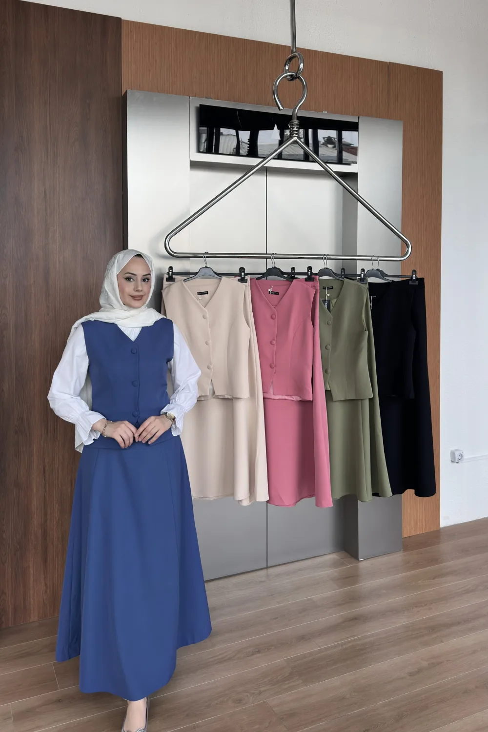 Model in the royal blue buttoned vest dress beside a rack showing the beige, rose, khaki and black colourways