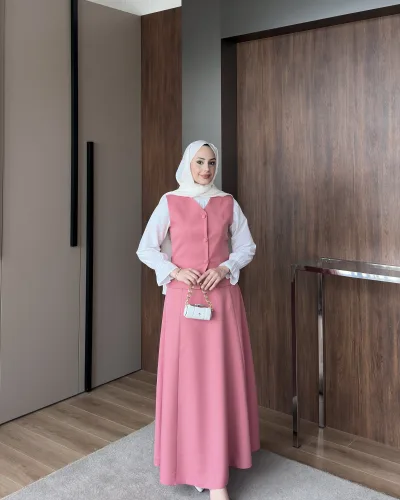 Model wearing a rose pink buttoned vest dress over a white blouse, full length with belted waist