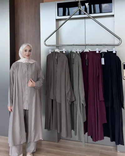Model in the taupe pleated shirt set beside a rack showing the khaki, olive, burgundy and black colourways
